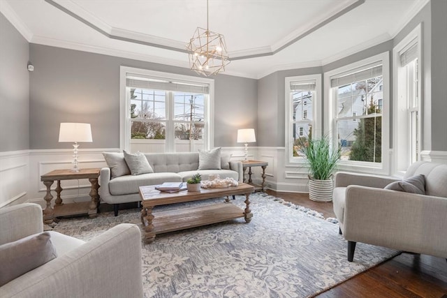 living room featuring a raised ceiling, an inviting chandelier, ornamental molding, and hardwood / wood-style flooring