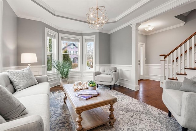 living room with a notable chandelier, a raised ceiling, crown molding, dark wood-type flooring, and ornate columns