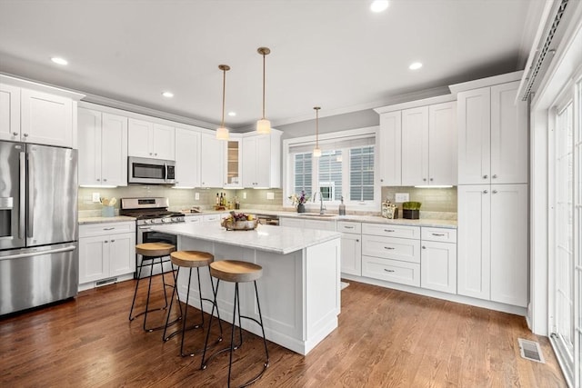 kitchen with appliances with stainless steel finishes, a kitchen island, decorative light fixtures, white cabinetry, and sink