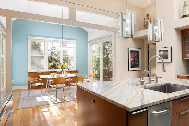 kitchen with sink, hanging light fixtures, light wood-type flooring, a kitchen island with sink, and light stone counters