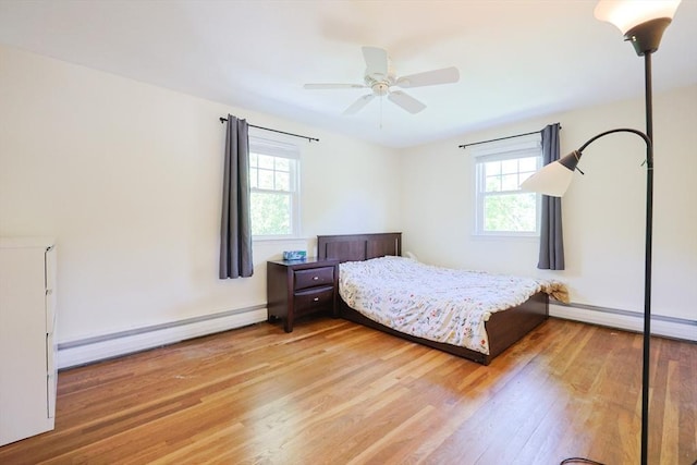 bedroom featuring a baseboard heating unit, multiple windows, and wood finished floors