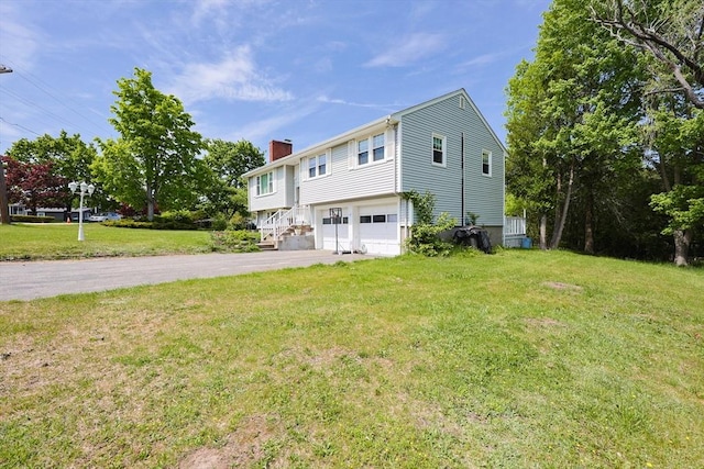 view of side of property featuring driveway, a chimney, a garage, and a lawn