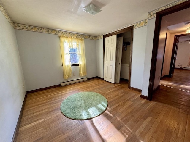 unfurnished bedroom with hardwood / wood-style flooring, a baseboard heating unit, and a closet