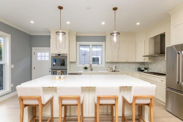 kitchen featuring decorative light fixtures, stainless steel appliances, a center island, and wall chimney exhaust hood