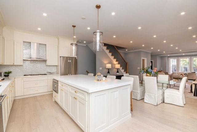 kitchen featuring appliances with stainless steel finishes, pendant lighting, decorative backsplash, a center island, and wall chimney range hood