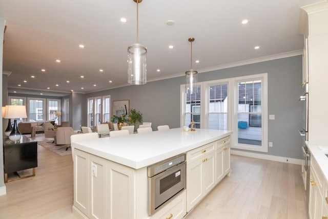 kitchen featuring light hardwood / wood-style flooring, ornamental molding, white cabinets, a kitchen island, and decorative light fixtures