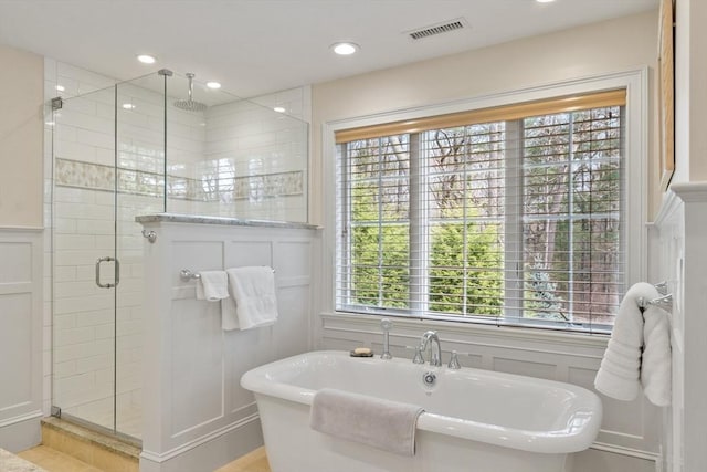 full bath featuring a decorative wall, a stall shower, a freestanding tub, wainscoting, and recessed lighting