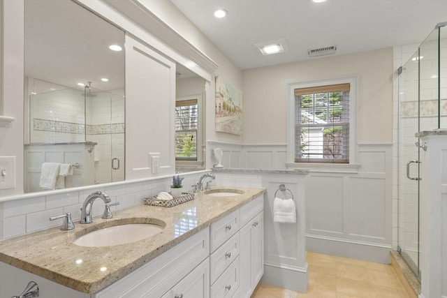 bathroom with a decorative wall, a stall shower, double vanity, recessed lighting, and wainscoting