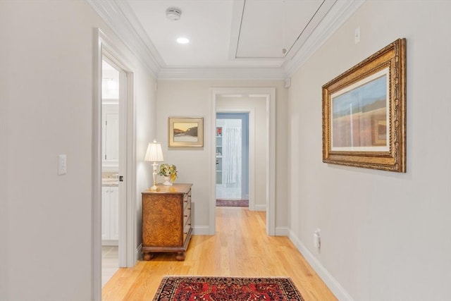 corridor with light wood-type flooring, attic access, ornamental molding, and baseboards
