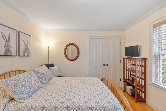 bedroom with light wood-type flooring, ornamental molding, a closet, and baseboards