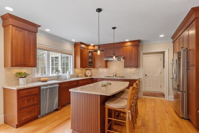 kitchen with appliances with stainless steel finishes, under cabinet range hood, a kitchen island, light wood-type flooring, and ornamental molding