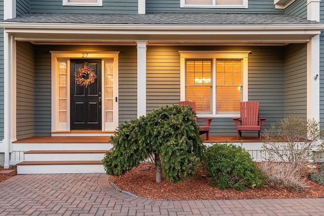 view of exterior entry with covered porch and a shingled roof