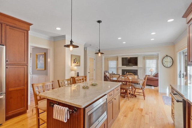 kitchen featuring appliances with stainless steel finishes, a breakfast bar, light wood-style floors, pendant lighting, and light stone countertops