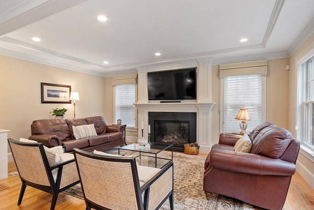 living area featuring light wood-style flooring, ornamental molding, recessed lighting, a fireplace, and a raised ceiling