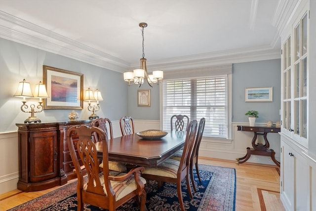dining room with a chandelier, wainscoting, crown molding, and light wood-style flooring