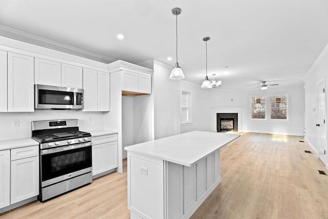 kitchen with stainless steel appliances, a fireplace, white cabinetry, light countertops, and crown molding