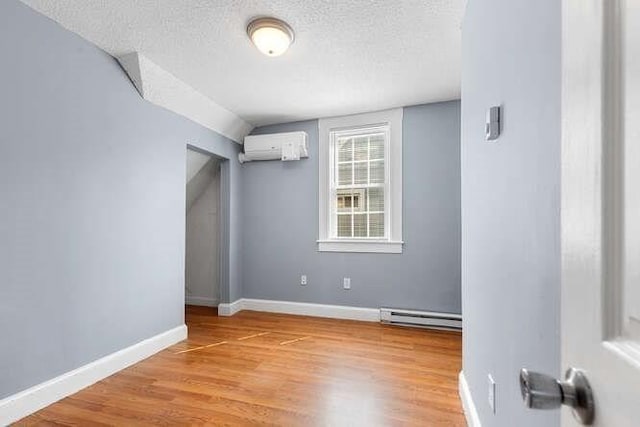 18 Anderson St, Lowell, MA 01852 - spare room with baseboard heating, a wall mounted AC, a textured ceiling, light wood-style flooring, and baseboards
