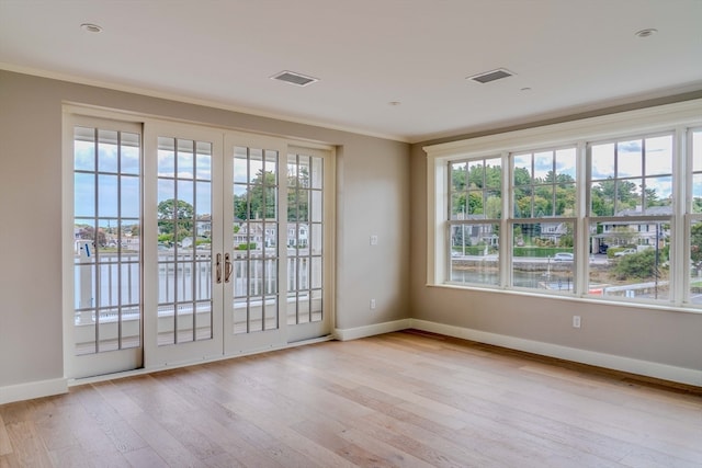 spare room featuring ornamental molding, plenty of natural light, light wood-type flooring, and french doors