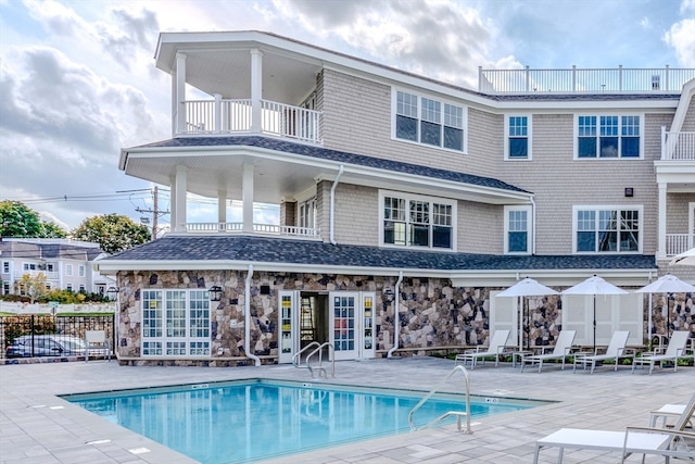 back of property featuring a balcony, a community pool, and a patio