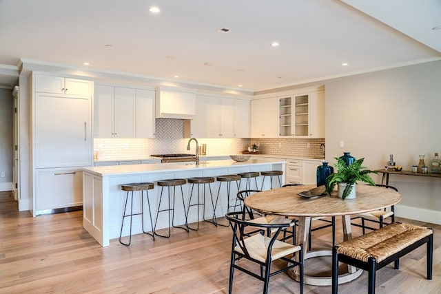 kitchen with white cabinetry, a center island with sink, crown molding, and light hardwood / wood-style flooring