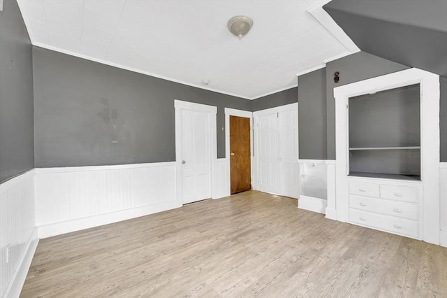 unfurnished living room featuring wood finished floors, a wainscoted wall, crown molding, and vaulted ceiling
