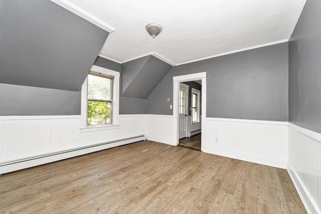 additional living space with a baseboard radiator, wood finished floors, a wainscoted wall, and vaulted ceiling