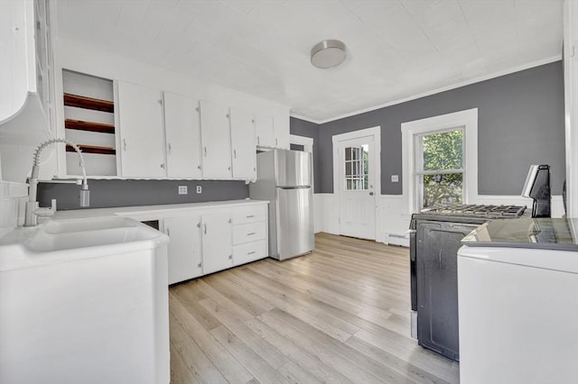 kitchen with freestanding refrigerator, a sink, white cabinetry, light wood-style floors, and crown molding