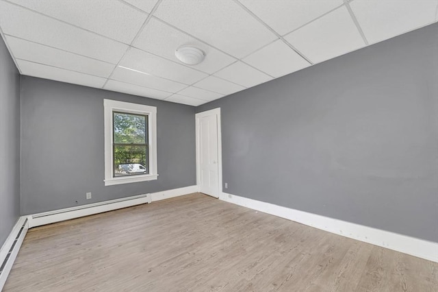 spare room with baseboard heating, a drop ceiling, wood finished floors, and baseboards