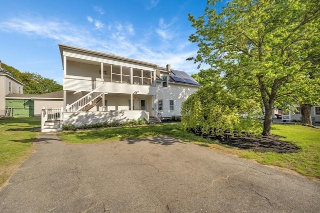view of front of home featuring stairs, a sunroom, and a front lawn