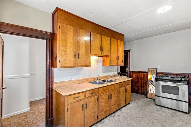 kitchen with light countertops, a sink, brown cabinets, wainscoting, and stainless steel gas range oven