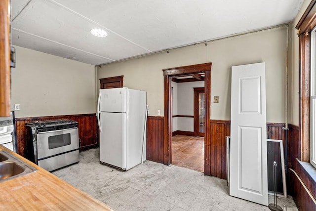 kitchen with freestanding refrigerator, a wainscoted wall, wooden walls, and stainless steel range with gas stovetop
