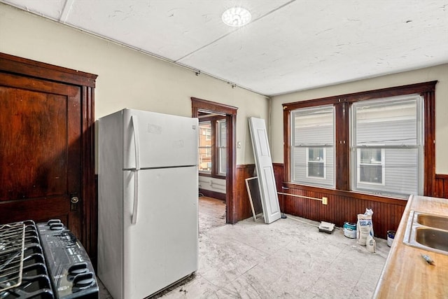 kitchen featuring wainscoting, wooden walls, light countertops, and freestanding refrigerator