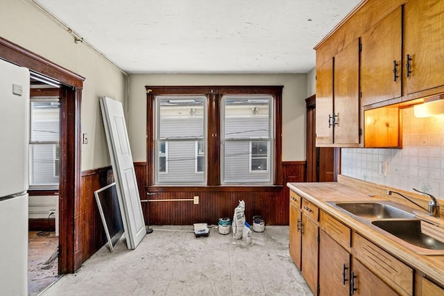 kitchen featuring light countertops, a sink, brown cabinetry, and wainscoting