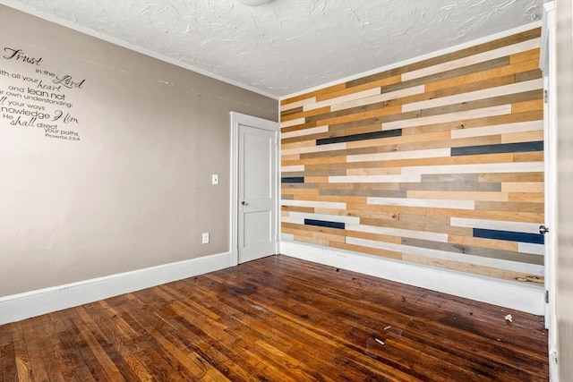 empty room featuring wooden walls, dark wood-style floors, baseboards, and a textured ceiling
