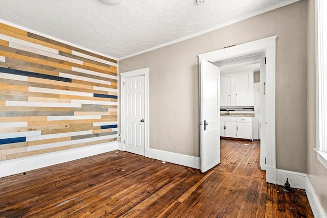 unfurnished bedroom with dark wood-style flooring, wooden walls, baseboards, ornamental molding, and a sink