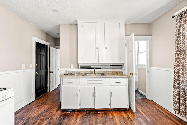 kitchen featuring a wainscoted wall, white cabinetry, a sink, and white stove