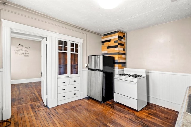 kitchen featuring a wainscoted wall, freestanding refrigerator, white gas range, a textured ceiling, and dark wood finished floors