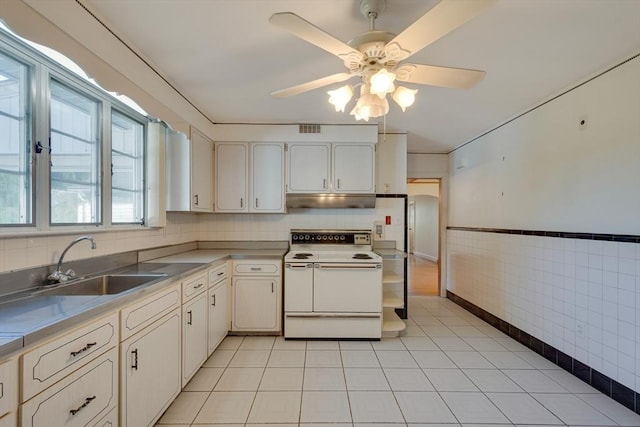 kitchen featuring under cabinet range hood, stainless steel countertops, light tile patterned floors, and white electric range