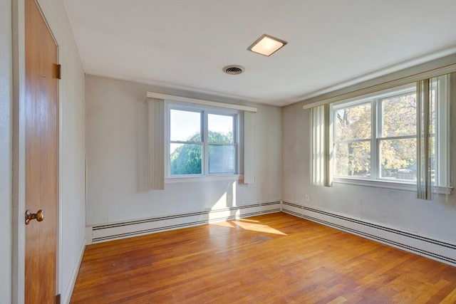 empty room with visible vents, plenty of natural light, baseboard heating, and wood finished floors