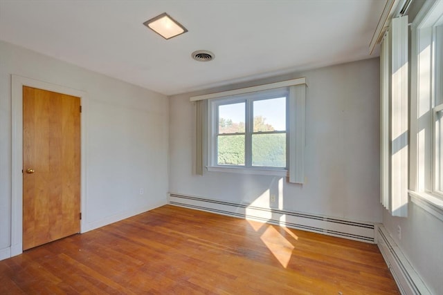 empty room with a baseboard radiator, wood finished floors, and visible vents