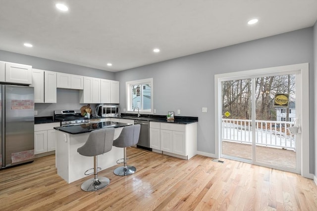 kitchen with a kitchen breakfast bar, white cabinets, stainless steel appliances, and light wood-type flooring