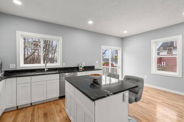 kitchen featuring dishwasher, sink, a kitchen island, light hardwood / wood-style flooring, and white cabinets