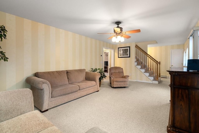 carpeted living area featuring a ceiling fan, stairway, baseboards, and wallpapered walls