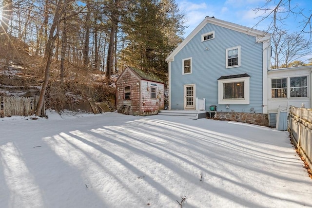 snow covered house featuring a storage unit, fence, and an outbuilding