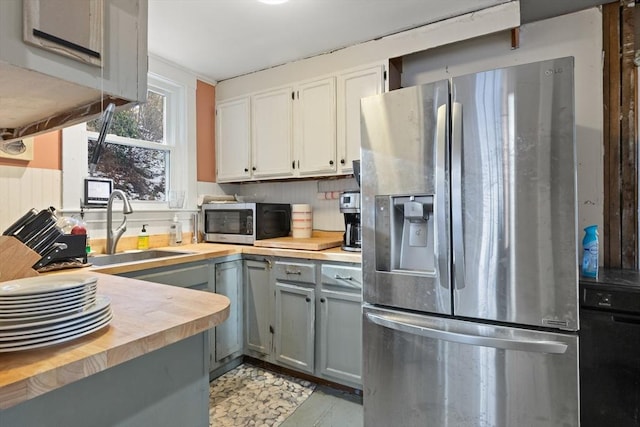 kitchen with gray cabinetry, stainless steel appliances, butcher block counters, a sink, and white cabinets