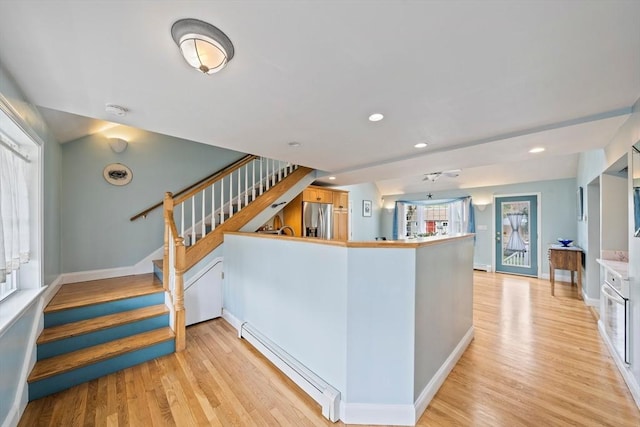 interior space featuring a baseboard radiator, stainless steel refrigerator with ice dispenser, light wood finished floors, and baseboards