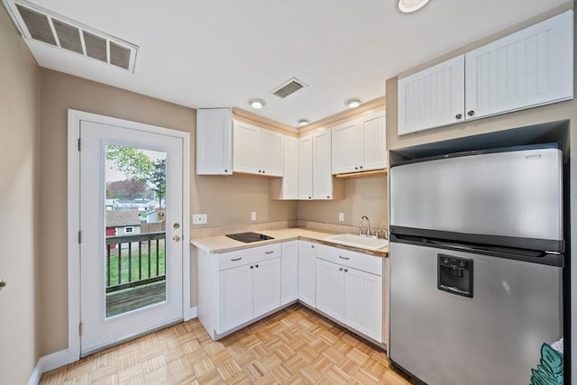 kitchen featuring a sink, stainless steel fridge, black electric cooktop, visible vents, and light countertops