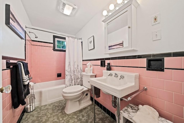 bathroom featuring a wainscoted wall, toilet, shower / bath combination with curtain, tile walls, and tile patterned floors