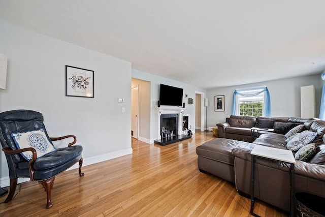living area featuring a fireplace with raised hearth, light wood finished floors, and baseboards