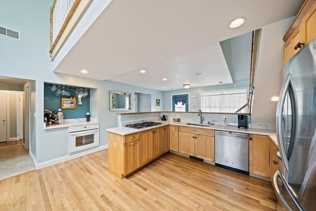 kitchen featuring appliances with stainless steel finishes, light countertops, a sink, visible vents, and a peninsula